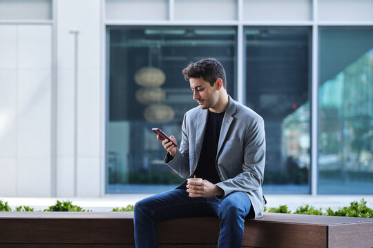 Young businessman using mobile phone drinking coffee break