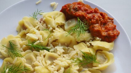 Tortellini with parmesan, ready to eat, Italian ravioli pasta with spinach and ricotta on white table, traditional italian food with herbs and vegetables