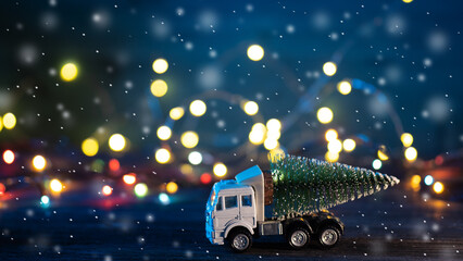 A toy truck transports a Christmas tree. Blue bokeh background with garland and falling snow.