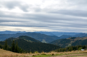 Fototapeta premium Expansive mountain valley with layered ridges, evergreen forests, and open meadows under a moody, cloud-filled sky. Carpathian Mountains, Ukraine