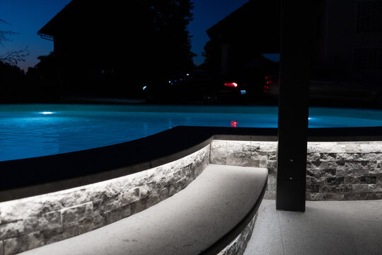 A modern outdoor pool glowing at night with vibrant LED lighting inside and around the water, creating a luxurious, serene, and atmospheric scene ideal for relaxation and nightlife visuals.