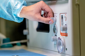 A person in a blue surgical gown is pressing a button on a machine