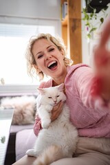 Woman laughing taking selfie with her white cat at home