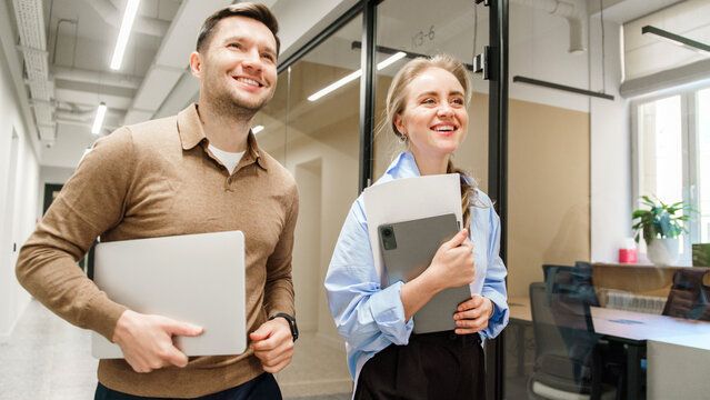 Office companions walking with laptops in a modern workspace