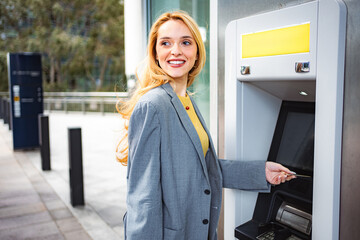 Happy young adult woman using ATM for cash withdrawal