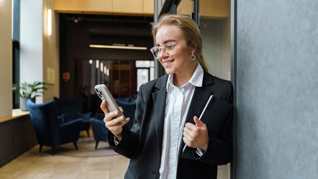 Woman checking phone while standing in modern office