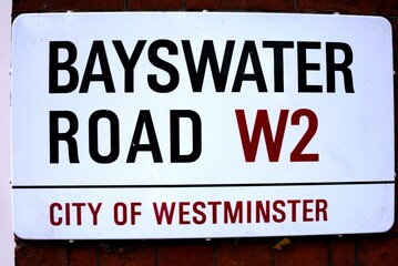 A close-up view of a Bayswater Road street sign mounted on a brick wall in the City of Westminster, London.