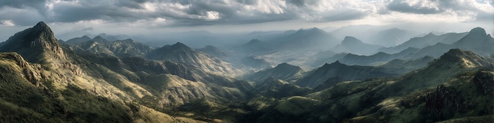 Fototapeta premium Aerial view of a vast mountain range under a cloudy sky with sunlight breaking through the clouds