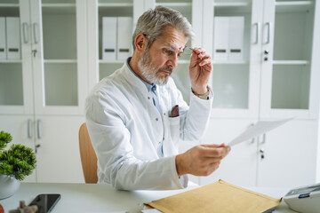 Male doctor carefully reading medical records in office