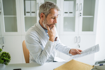Mature doctor reading medical report in hospital office