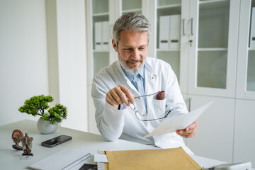 Mature doctor man analyzing medical report in office