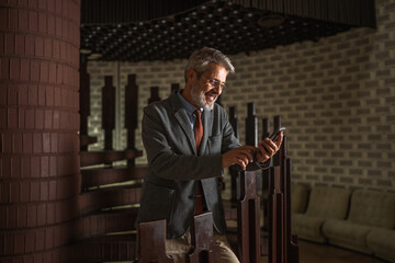 Mature businessman smiling, holding mobile phone in modern building