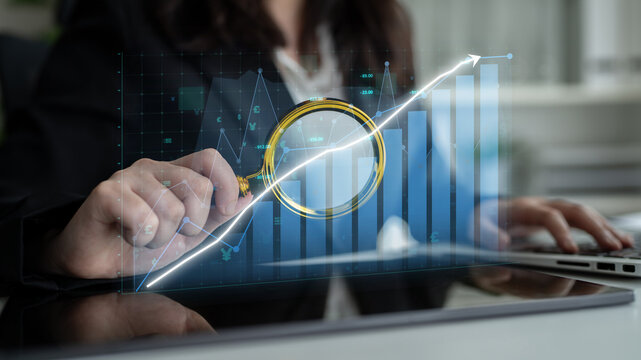 A businessperson uses a magnifying glass to examine financial growth trends displayed on a digital graph in a modern office setting, highlighting the importance of data analysis. Impute