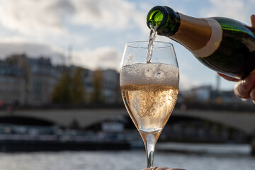 Pouring and drinking of french sparkling wine champagne from tulip glasses with view on Paris streets, buildings, Seine river embarkment, boats, bridges, wedding event in Paris © barmalini