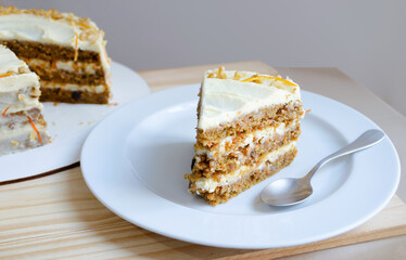 Rebanada de pastel de zanahoria en primer plano, servida en un plato blanco con cucharita de postre.