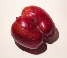 An ugly red apple. A fruit with a shape flaw on a white background.