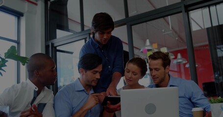 Working team in business casual leaning over laptop and tablet at open-plan office, with coffee cup