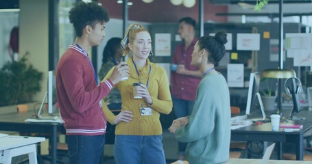 Talking coworkers in maroon, mustard, teal sweaters, standing in open office with coffee, lanyards