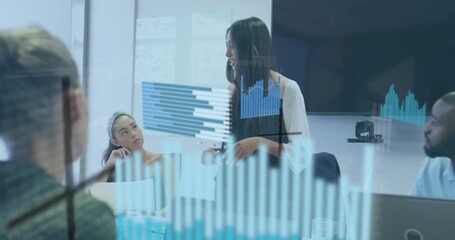 Presenting woman in business casual gesturing toward data charts on glass in conference room