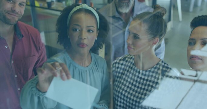 Reaching woman wearing light-blue blouse and pale headband placing paper on glass board in office