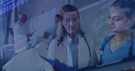 Reviewing doctor in white coat and nurse in blue scrubs checking chart at ward, stethoscopes