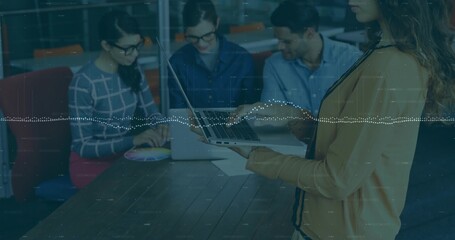 Presenting standing woman in tan cardigan holding laptop at meeting table, data overlay, copy space