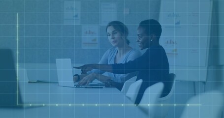 Pointing right and typing left women in business attire at table with laptop and flip chart