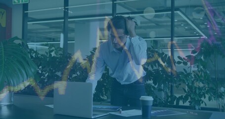 Leaning man in white shirt studying laptop and reports in office with financial overlay, coffee cup