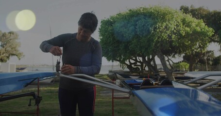 Adjusting older woman wearing grey top fixing rigger on blue rowing shell at boatyard, copy space