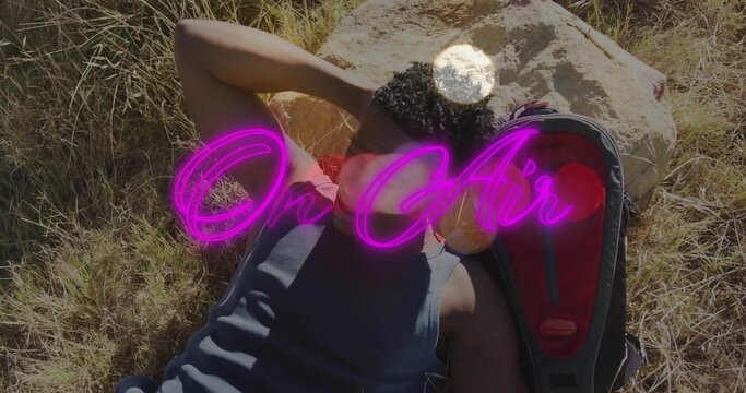 Reclining man wearing tank top on grass by pale rock, red-lined backpack, magenta On Air overlay