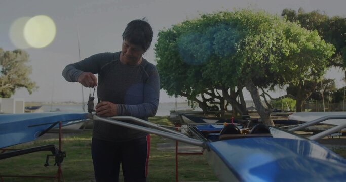 Adjusting older woman wearing grey top fixing rigger on blue rowing shell at boatyard, copy space - Powered by Adobe