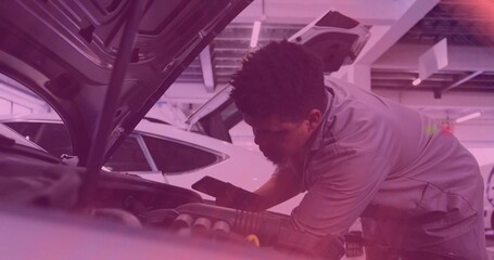 Leaning mechanic in gray work shirt inspecting engine bay under raised hood at shop, holding phone
