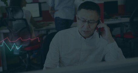 Holding phone, man wearing light shirt looking at monitor at desk with red chairs, chart