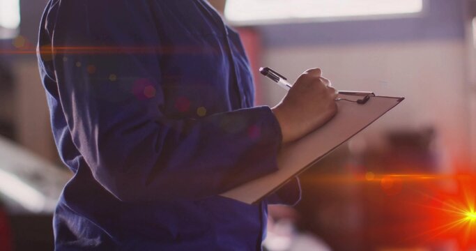 Holding clipboard female technician wearing blue coverall writing notes at workshop with pen - Powered by Adobe