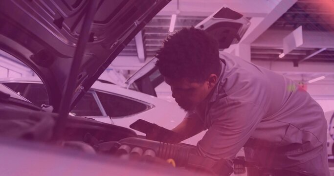 Leaning mechanic in gray work shirt inspecting engine bay under raised hood at shop, holding phone