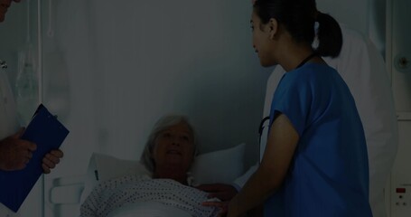 Reclining senior patient receiving touch from nurse in blue scrubs at bedside, wearing dotted gown