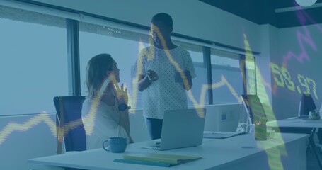 Two midadult women discussing financial charts in office, white top, light blouse, laptop and phone