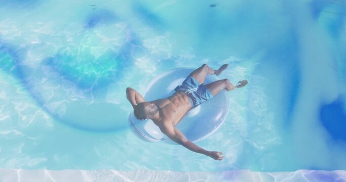 Floating man in blue trunks reclining on clear inflatable ring in private pool, visible pool edge