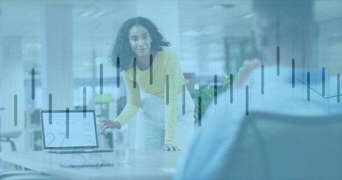 Pointing presenter wearing yellow top, light trousers leaning at office with laptop chart overlay - Powered by Adobe