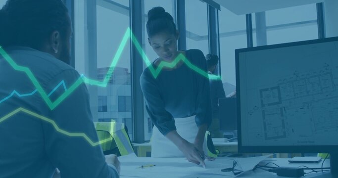 Pointing woman architect wearing dark top and light skirt leaning at office table, with plans, vest