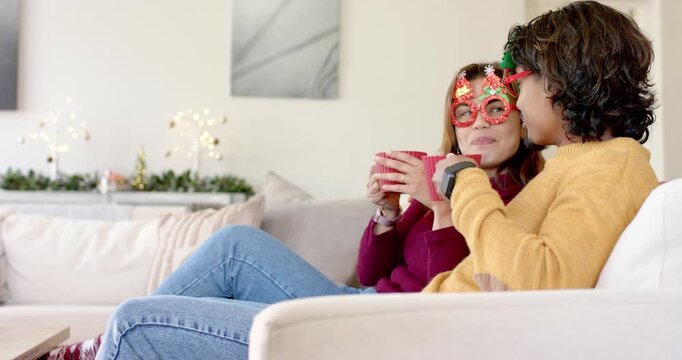 Couple settling on couch at home celebrating holiday by lifting red mugs, sipping drink, copy space