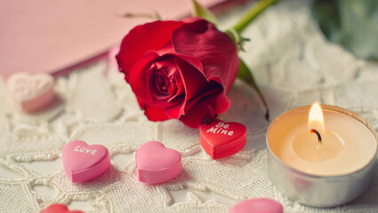 Red rose, heart shaped candies with love and be mine text, and a burning tea light candle creating a romantic atmosphere for valentine's day celebration