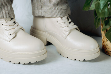 A pair of beige boots with trousers on a cement background.
