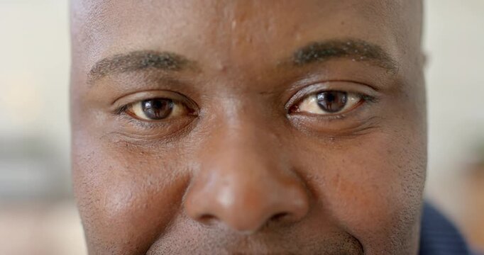Blinking and holding gaze, mid-adult African American man forming gentle smile in soft interior