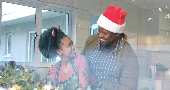 African American couple exchanging shoulder touch sharing laughter by garland on kitchen counter