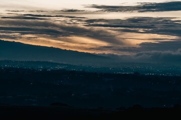 Fototapeta premium Sunrise illuminates the landscape as distant lights twinkle in the early morning haze over the hills