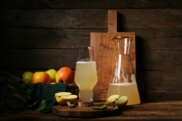 Glass and jug of fresh apple kvass on wooden background