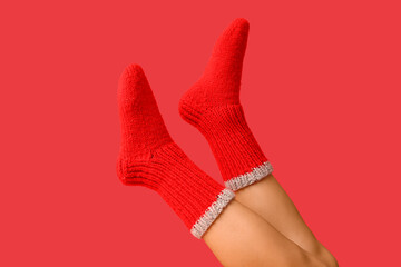 Legs of young woman in red knitted socks on color background