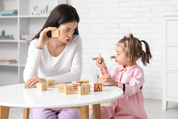 Female teacher with cubes and little girl learning alphabet at home