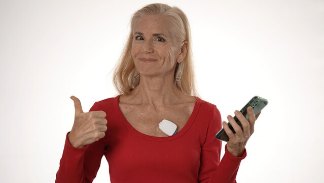 Mature woman gives a thumbs up while wearing a heart monitor and holding a smartphone to manage her atrial fibrillation and health